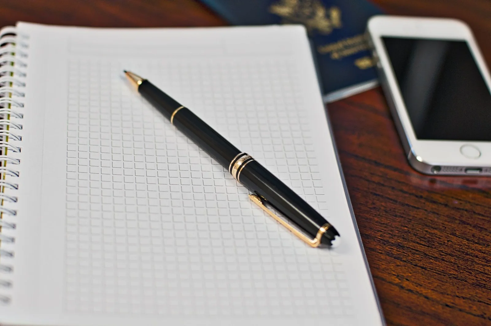 A smartphone, passport and notebook arranged on a wooden table for travel planning.